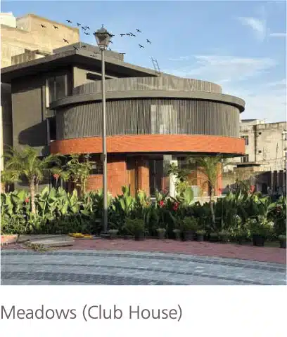 Meadows clubhouse exterior with curved modern façade, landscaped greenery, and paved arrival plaza in Zirakpur